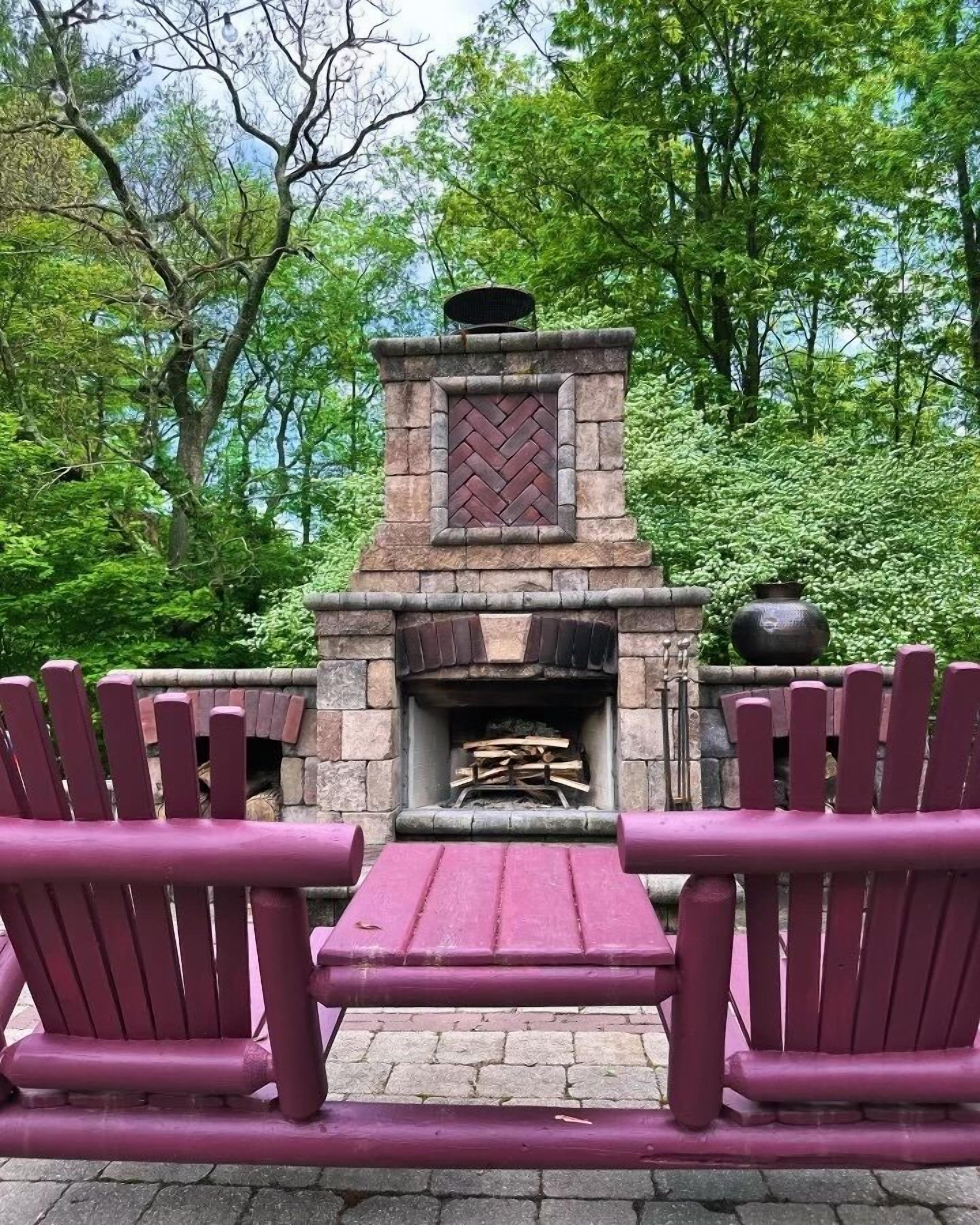A stone outdoor fireplace with a herringbone pattern, flanked by two Adirondack chairs.