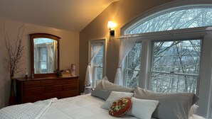 Een slaapkamer met een groot bed, een dressoir, een spiegel en een raam met gordijnen.