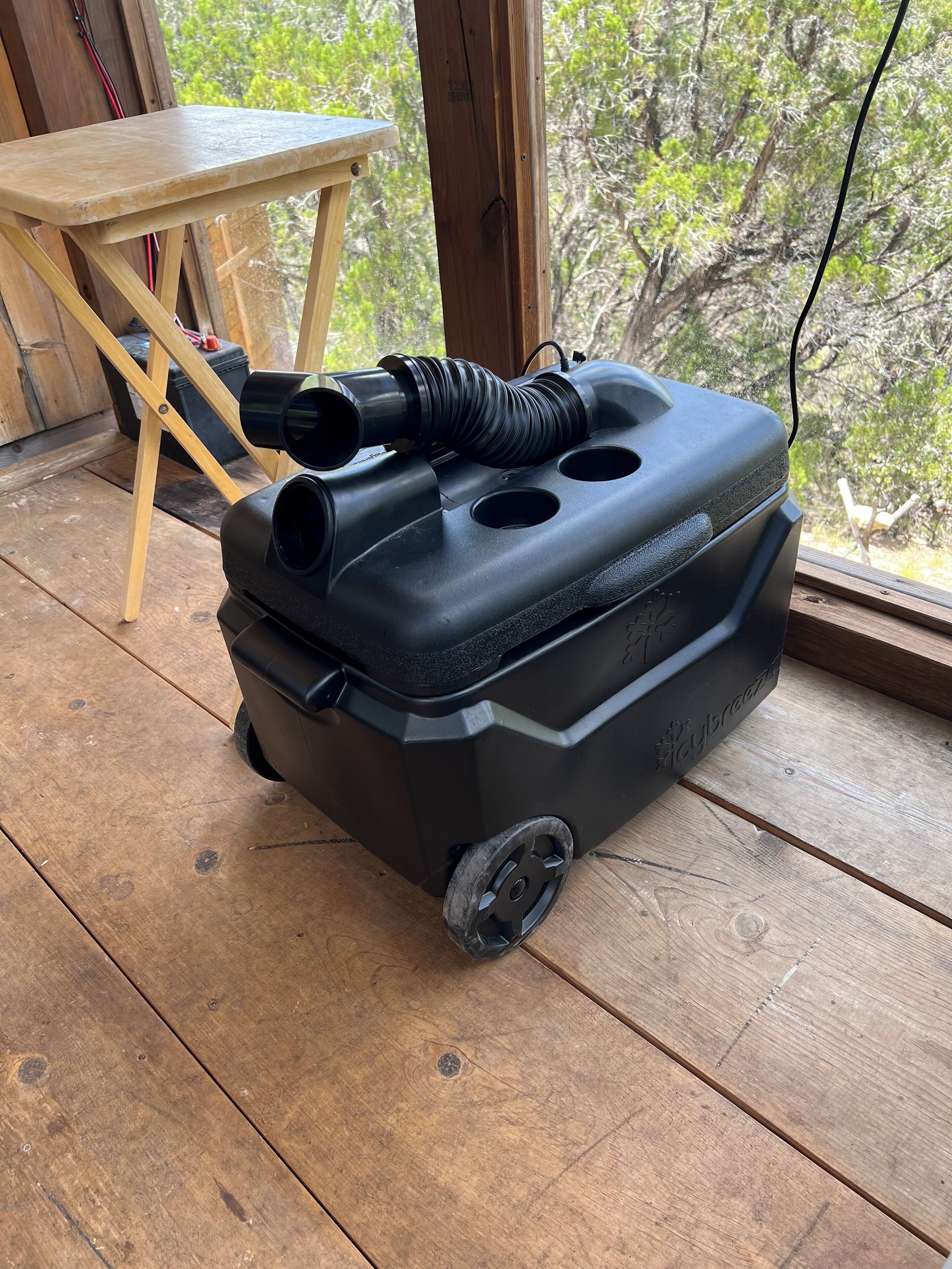 A portable air compressor on a wooden deck with a table and chair in the background.