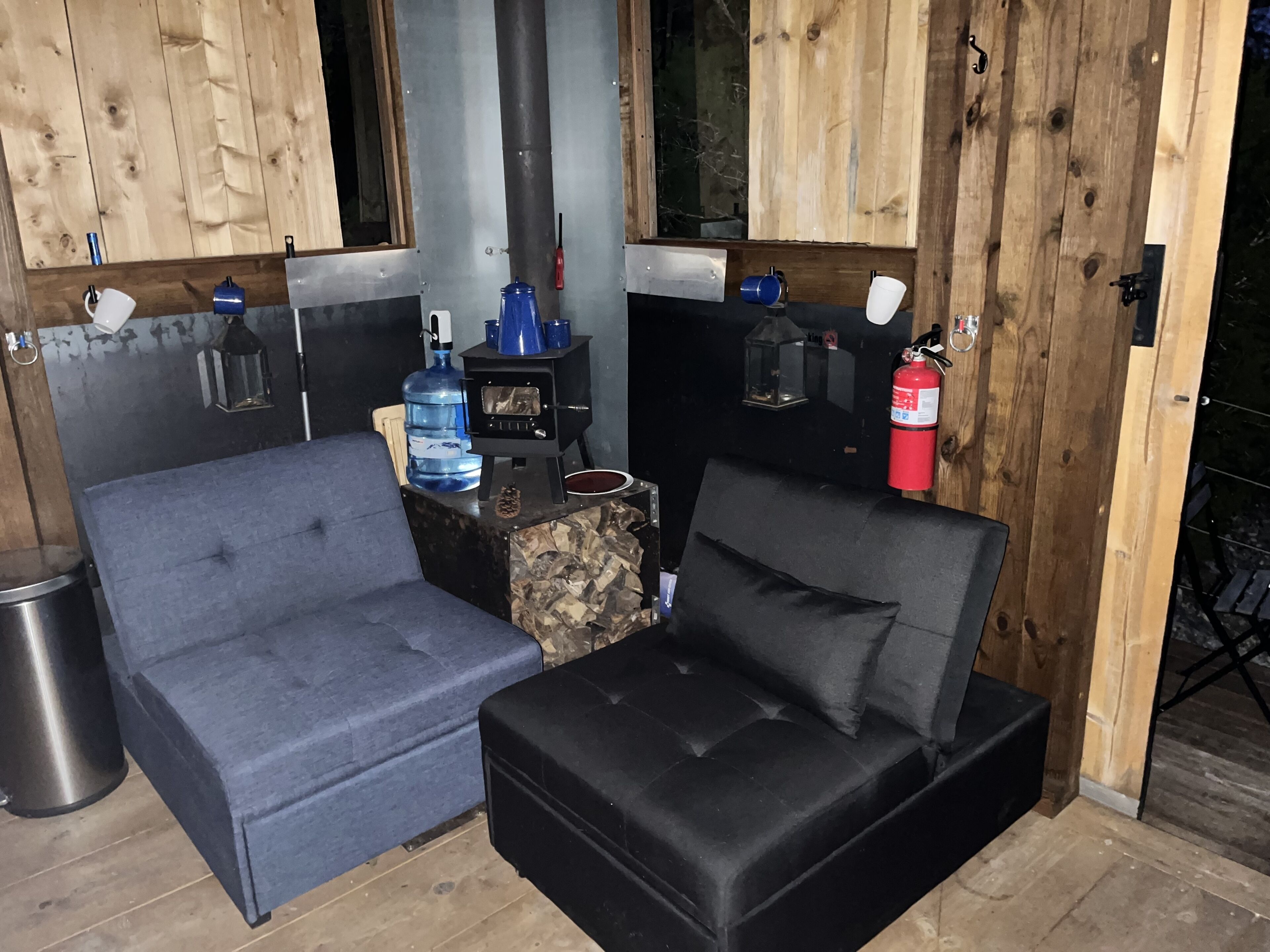 A cozy outdoor seating area with two sofas, a water dispenser, and a fire pit.