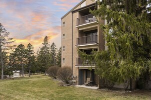 Un edificio de apartamentos de varios pisos con fachada de ladrillo, balcones y un césped con árboles.