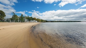 A beach with a sandy shore, a calm body of water, and a clear sky with clouds. - Lakeview Golf Retreat 1BDR Condo 5057 (Williamsburg)