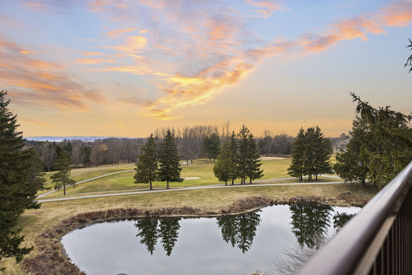 Une vue d’un parc avec un étang, des arbres et un coucher de soleil.