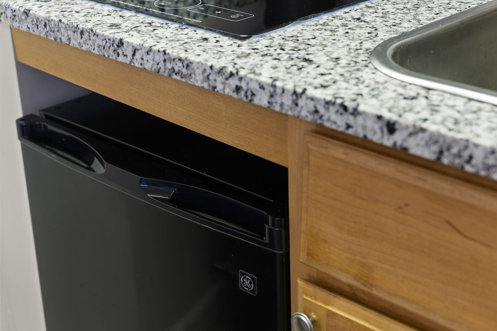 Una cocina con encimera de granito, lavavajillas y armarios de madera.