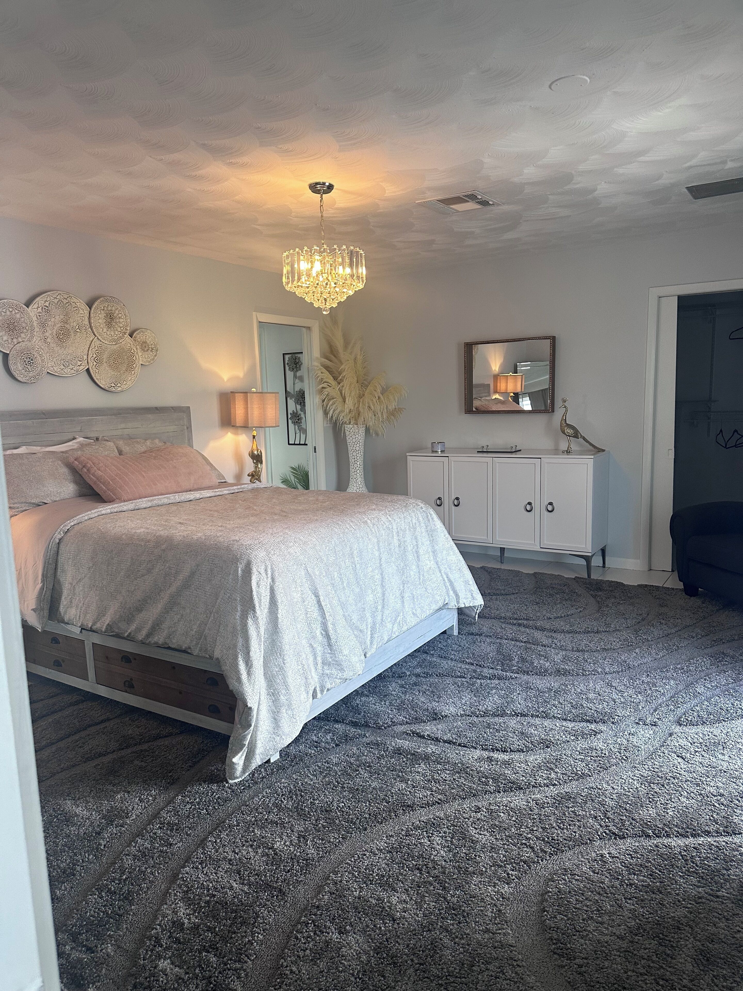 Een slaapkamer met een bed, een dressoir, een spiegel en een kroonluchter.