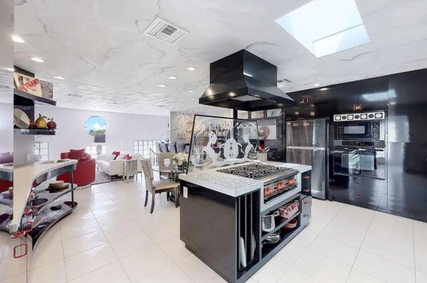 Una cocina moderna con una isla central, hornos integrados y un comedor con mesa blanca y sillas rojas.