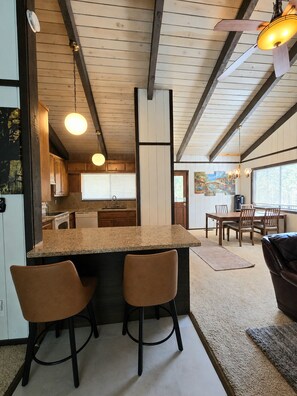 A modern kitchen with a central island, bar stools, and a dining area with a table and chairs.