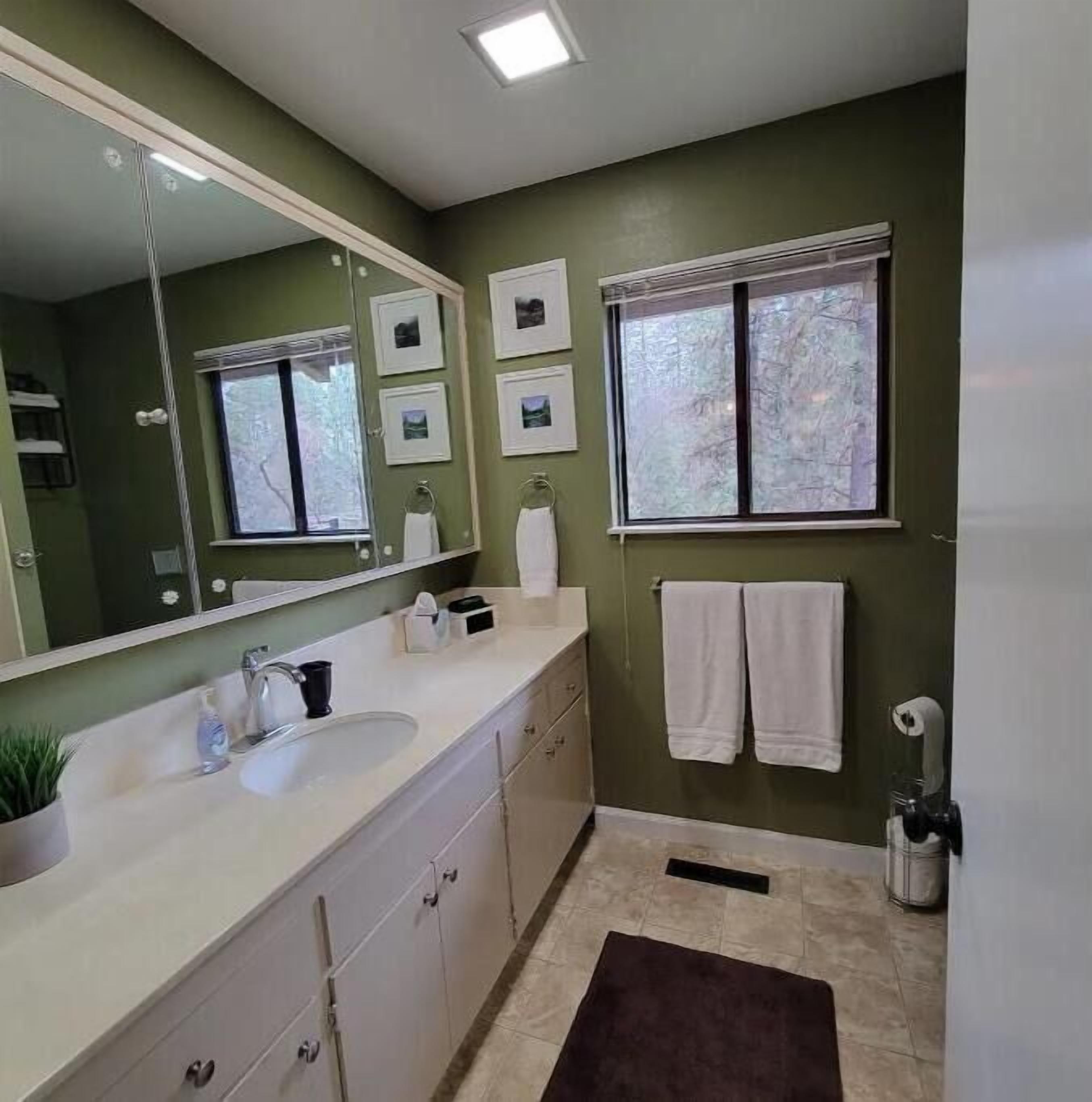 Un baño con un espejo grande, un lavabo, una ventana y un perchero para toallas.