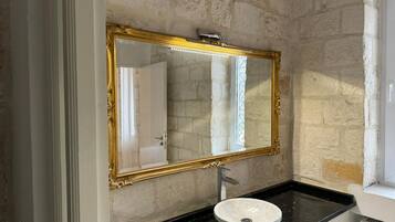 A bathroom with a stone wall, a gold-framed mirror, a white sink, and a black countertop.