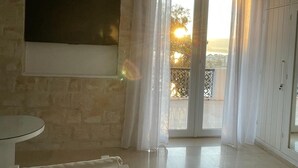 Una habitación con pared de piedra, un televisor de pantalla plana montado en ella, un balcón con cortinas blancas y vistas al exterior.