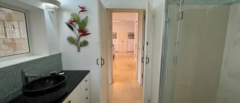 A narrow hallway with a bathroom on the left, featuring a black sink and a mirror.
