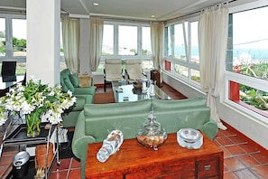 A spacious living room with a green sofa, a coffee table, and a view of the sea.