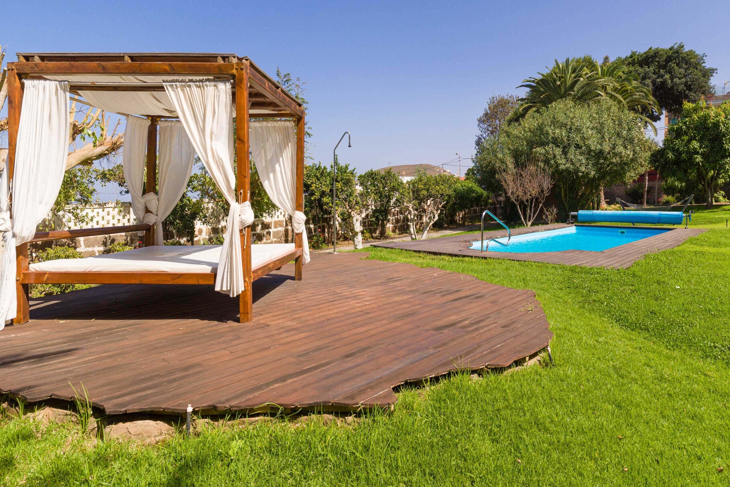 Una terraza de madera con una cama con dosel y una piscina al fondo.