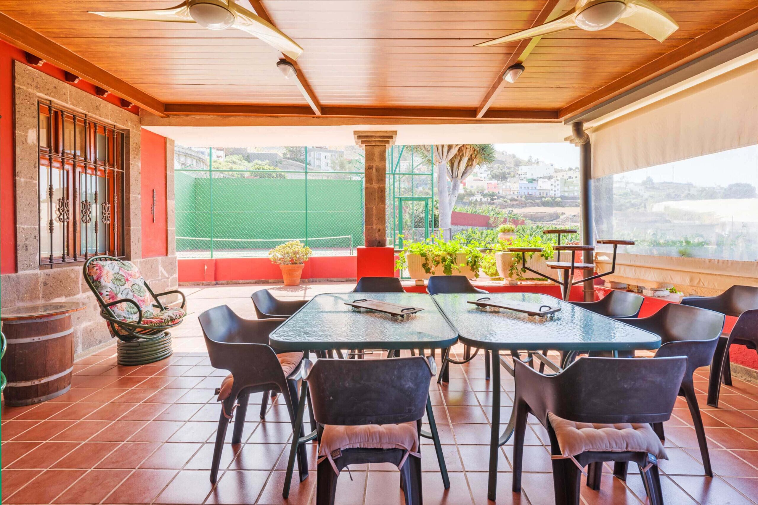 An outdoor patio with a wooden ceiling, tiled floor, and several tables and chairs.