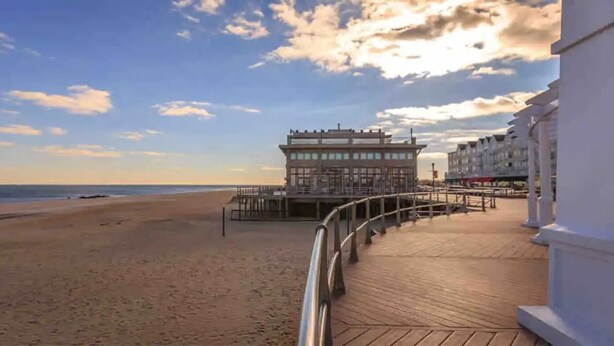 A beachside promenade with a boardwalk leading to a building with a balcony overlooking the ocean.