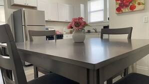A modern kitchen with white cabinets, a stainless steel refrigerator, and a dining table with four chairs.