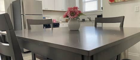 Une cuisine moderne avec des meubles blancs, un réfrigérateur en acier inoxydable et une table à manger avec quatre chaises.