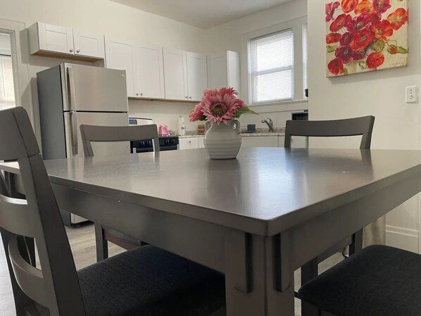 A modern kitchen with white cabinets, a stainless steel refrigerator, and a dining table with four chairs.