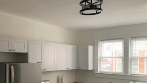 A modern kitchen with white cabinets, stainless steel appliances, a built-in oven, and a window with blinds.