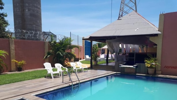 Una piscina con muelle de madera, sillas blancas y una zona de estar cubierta.