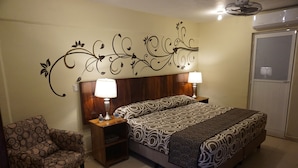 Un dormitorio con una cama, dos mesitas de noche con lámparas, una silla y un diseño decorativo en la pared.