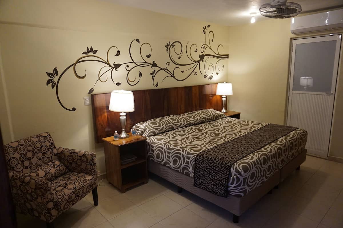 A bedroom with a bed, two bedside tables with lamps, a chair, and a decorative wall design.