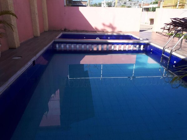 A swimming pool with a blue interior, surrounded by a pink wall and a wooden deck.