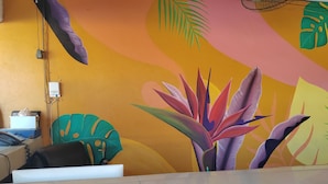 Una habitación con un vibrante mural de plantas tropicales en la pared, un escritorio con una computadora y una silla.