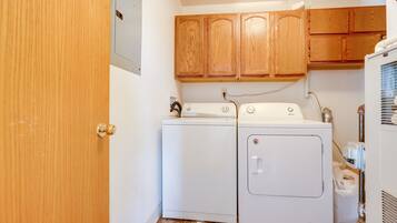 A laundry room with two white washing machines, wooden cabinets above, and a door to the left.