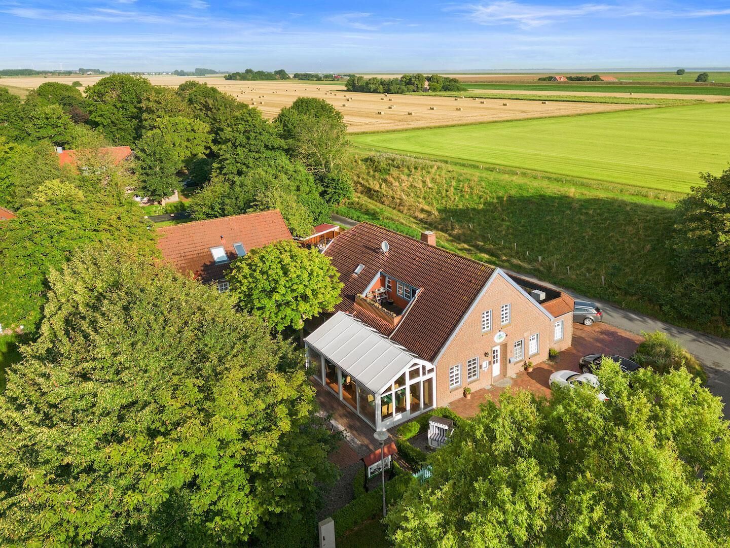 Een landhuis met een grote tuin en velden op de achtergrond.