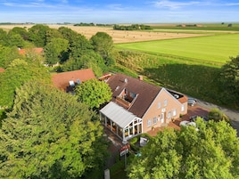 Una casa rural con un jardín grande y campos en el fondo.