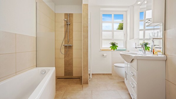 A modern bathroom with a bathtub, shower, toilet, and sink. - Hotel Deichinsel (Wangerland)