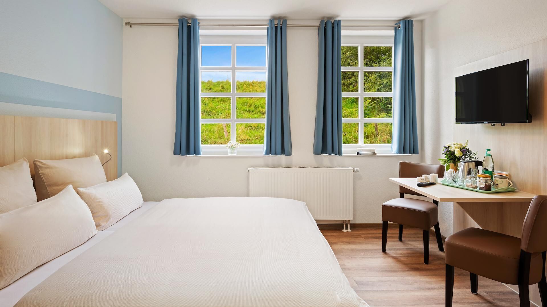 Una habitación de hotel con una cama grande, un escritorio con silla, un televisor y ventanas con cortinas.