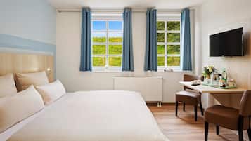 Una habitación de hotel con una cama grande, un escritorio con silla, un televisor y ventanas con cortinas.