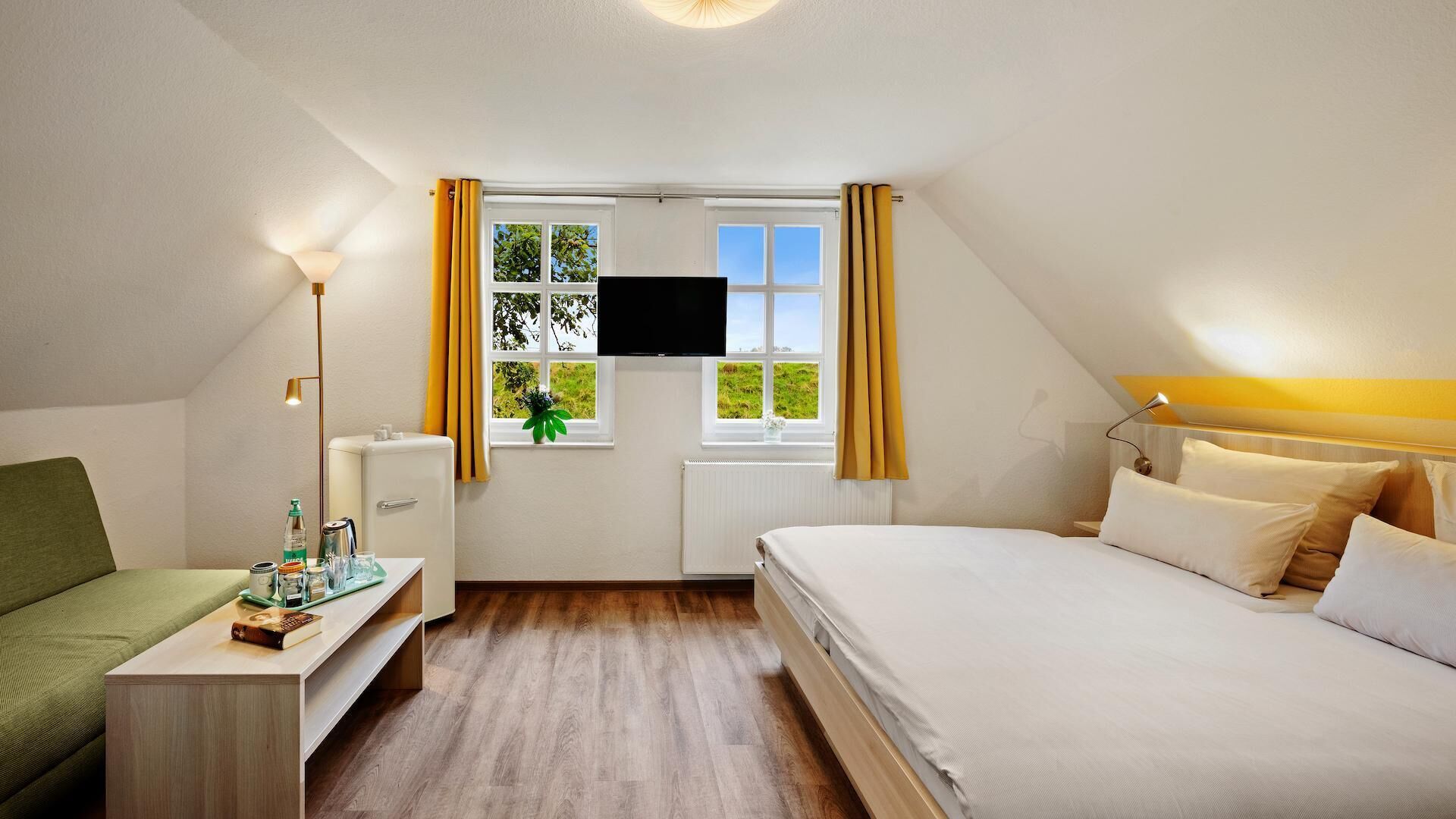 Une chambre à coucher avec un lit, un bureau, une chaise, une télévision et une fenêtre avec des rideaux.