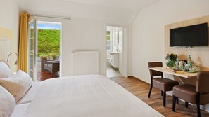 A hotel room with a large bed, a desk with chairs, a television, and a view of a garden through an open door. - Hotel Deichinsel (Wangerland)