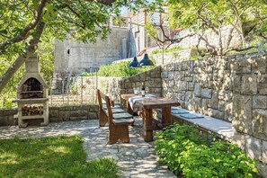 Eine Terrasse im Freien mit Steinmauern, Holztischen und -stühlen sowie einem Holzofen.