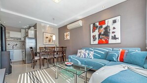 A modern living room with a blue sofa, a glass coffee table, and a dining area with wooden chairs. - Magical Garden with Shared Jacuzzi - Blanka A2 (Banjol)