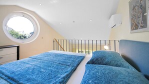 A bedroom with a skylight, a bed with blue bedding, a nightstand, and a wall-mounted air conditioner. - Magical Garden with Shared Jacuzzi - Blanka C2 (Banjol)