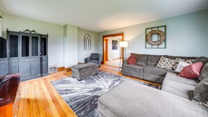 Una sala de estar con un mueble de madera oscura, un sofá gris, un tapete estampado y un reposapiés gris.