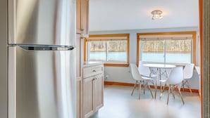 A modern kitchen with a stainless steel refrigerator, wooden cabinets, and a dining area with white chairs and a table. - Lakefront Salem Retreat - Fish, Swim, Kayak & More (Salem)