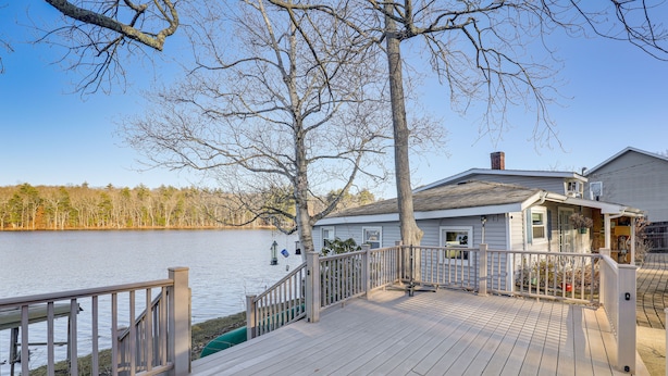 A wooden deck with a railing overlooking a body of water, a house with a chimney, and a clear sky. - Lakefront Salem Retreat - Fish, Swim, Kayak & More (Salem)