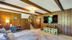 Ein Wohnzimmer mit Holzwänden, einer Couch, einem Fernseher und einer Treppe, die in einen anderen Raum führt.