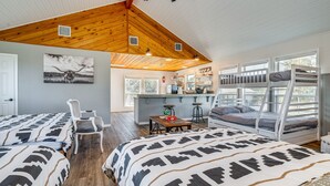 A cozy room with two beds, a wooden ceiling, a dining area, and a view through large windows. - Expansive Bertram Retreat w/ Pool, on 28 Acres! (Bertram)