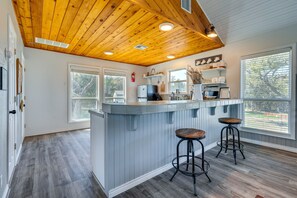 A kitchen with a wooden ceiling, a bar area with stools, and a view through large windows. - Expansive Bertram Retreat w/ Pool, on 28 Acres! (Bertram)