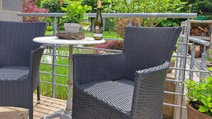 A patio area with wicker chairs and a table, surrounded by greenery and a stone wall.