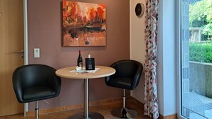 A room with two black chairs around a small round table, a painting on the wall, and a window with a view of greenery.