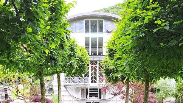 A pathway leading to a building with a modern architectural design, surrounded by lush greenery and trees.