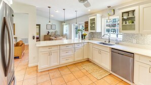 A modern kitchen with white cabinets, a stainless steel dishwasher, and a ceiling fan. - Gas Grill & Fire Pit: Peaceful Dunnellon Home! (Dunnellon)