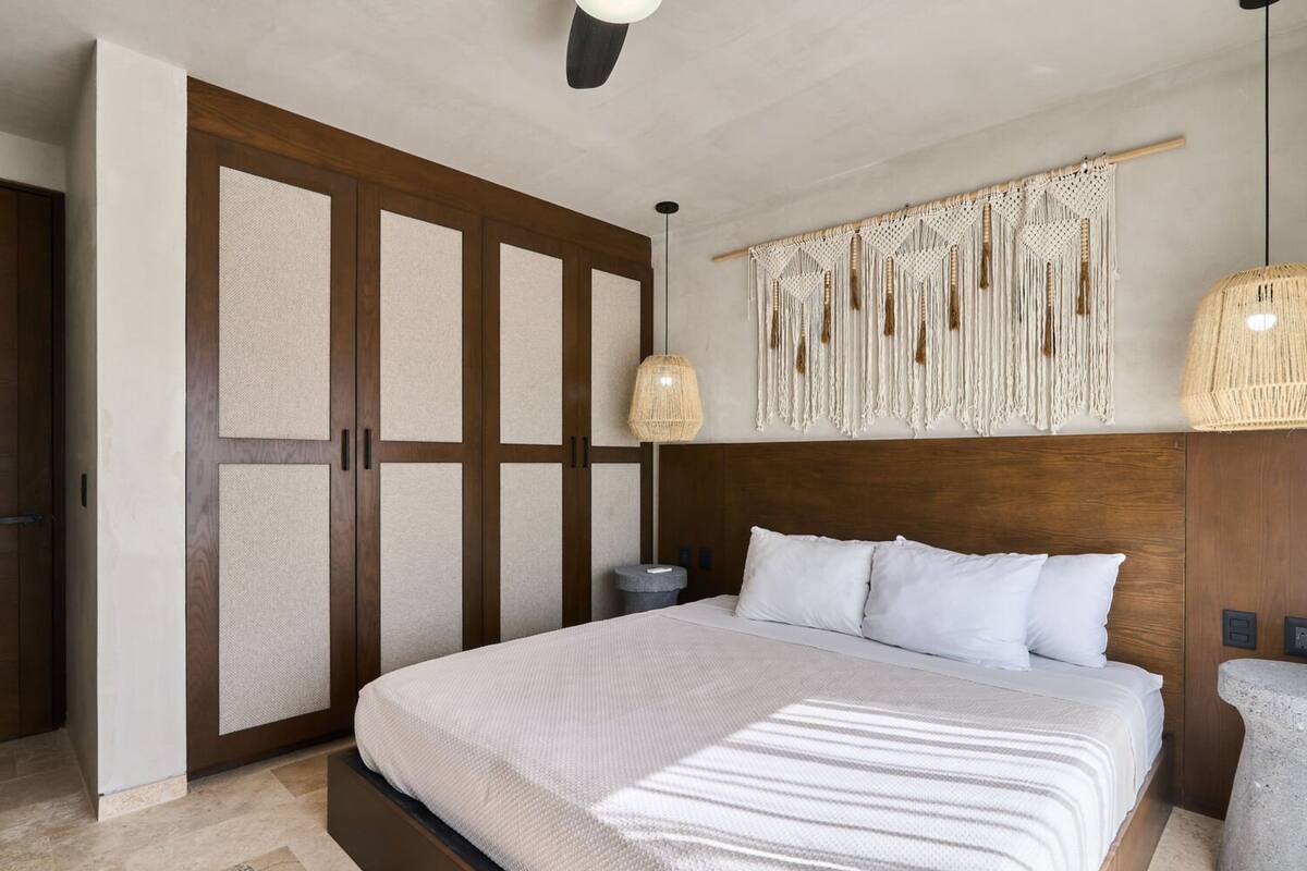 A modern bedroom with a large bed, wooden headboard, and a macrame wall hanging.